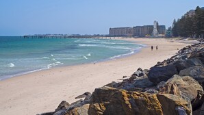 A beach with a rocky shoreline, a pier extending into the ocean, and a large hotel in the background. - Beachfront Serenity Glenelg (Glenelg)