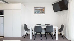 A modern room with a white table, four black chairs, a flat-screen TV on the wall, and a framed picture above the table. - Beachfront Serenity Glenelg (Glenelg)