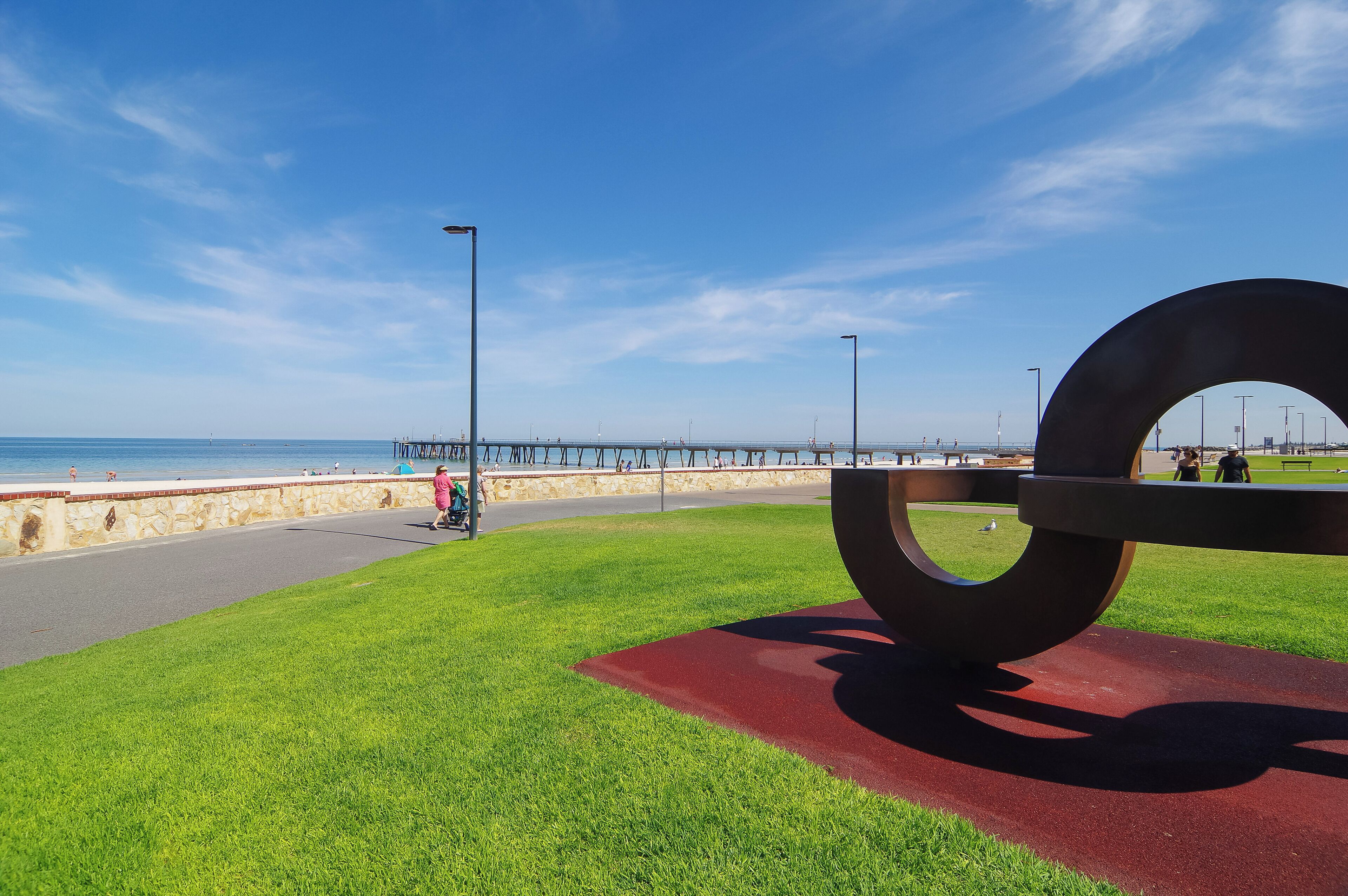 Un parc doté d’une grande sculpture métallique, d’une allée pavée et d’une jetée située au loin.
