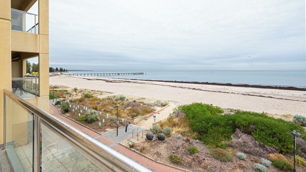 A beach view from a balcony with a clear sky, sandy beach, and a pier in the distance. - Beachfront Serenity Glenelg (Glenelg)