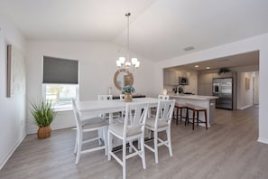 A modern kitchen with white cabinetry, a central island with bar stools, and a hanging light fixture. - Whispering Palm Breeze Cottage at Eastport - 3/2 w/ PRIVATE POOL in The Village of Moultrie Creek (Moultrie Creek, The Villages)