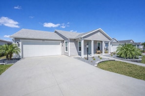 A two-story house with a garage, a covered porch, and a well-maintained lawn. - Whispering Palm Breeze Cottage at Eastport - 3/2 w/ PRIVATE POOL in The Village of Moultrie Creek (Moultrie Creek, The Villages)