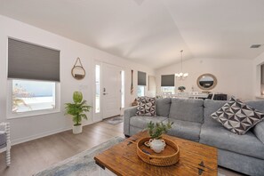 A modern living room with a grey sofa, a wooden coffee table, and a potted plant. - Whispering Palm Breeze Cottage at Eastport - 3/2 w/ PRIVATE POOL in The Village of Moultrie Creek (Moultrie Creek, The Villages)
