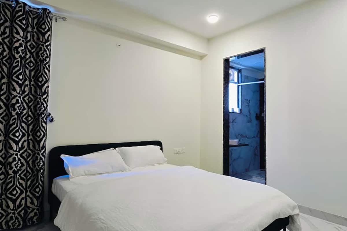 A bedroom with a bed, a ceiling fan, and a patterned curtain.