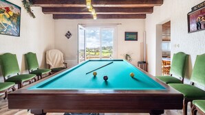 Una mesa de billar con sillas, un cuadro y vistas al exterior.