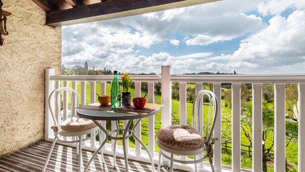 Un balcón con mesa y sillas, vista a un paisaje verde y cielo nublado.
