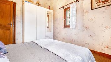 Una camera da letto con un letto, un armadio, una finestra con tende e una parete con carta da parati a motivi floreali.
