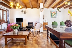 Un salon avec un plafond en bois, un téléviseur, un canapé, un fauteuil, une table ornée d’un vase de fleurs et une horloge au mur.
