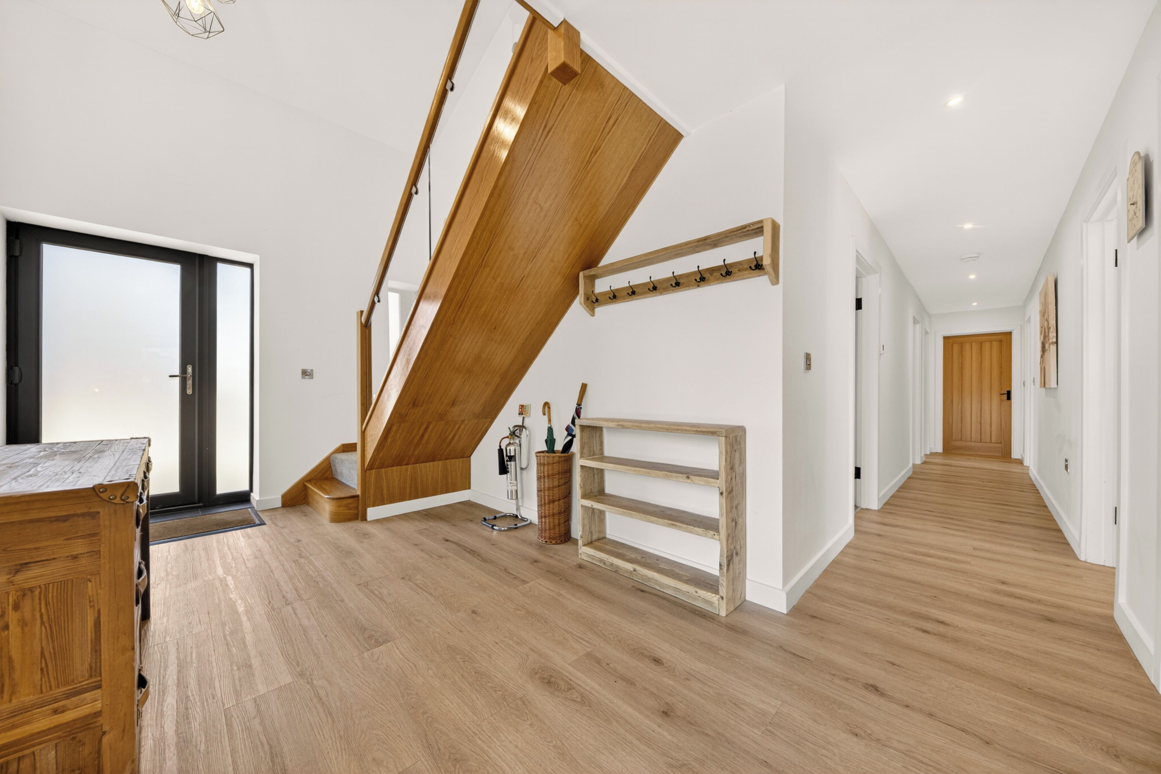 Un interior moderno con una escalera de madera, un banco de madera y un pasillo que lleva a una puerta.