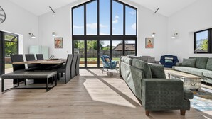 Une pièce spacieuse dotée d’une grande fenêtre, d’un coin repas et d’un espace détente avec un canapé et des fauteuils.