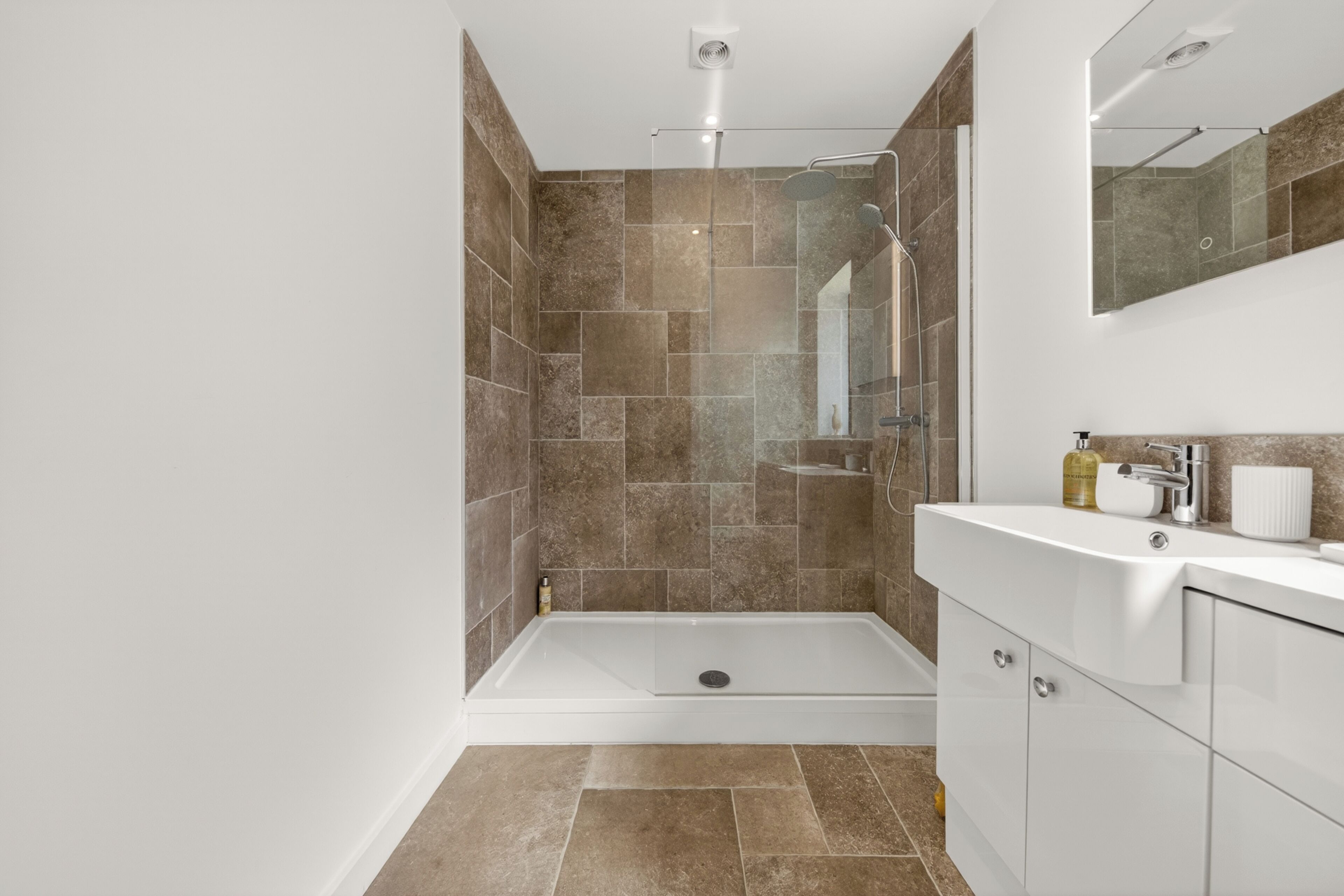 A modern bathroom with a glass-enclosed shower, a white vanity, and a large mirror.