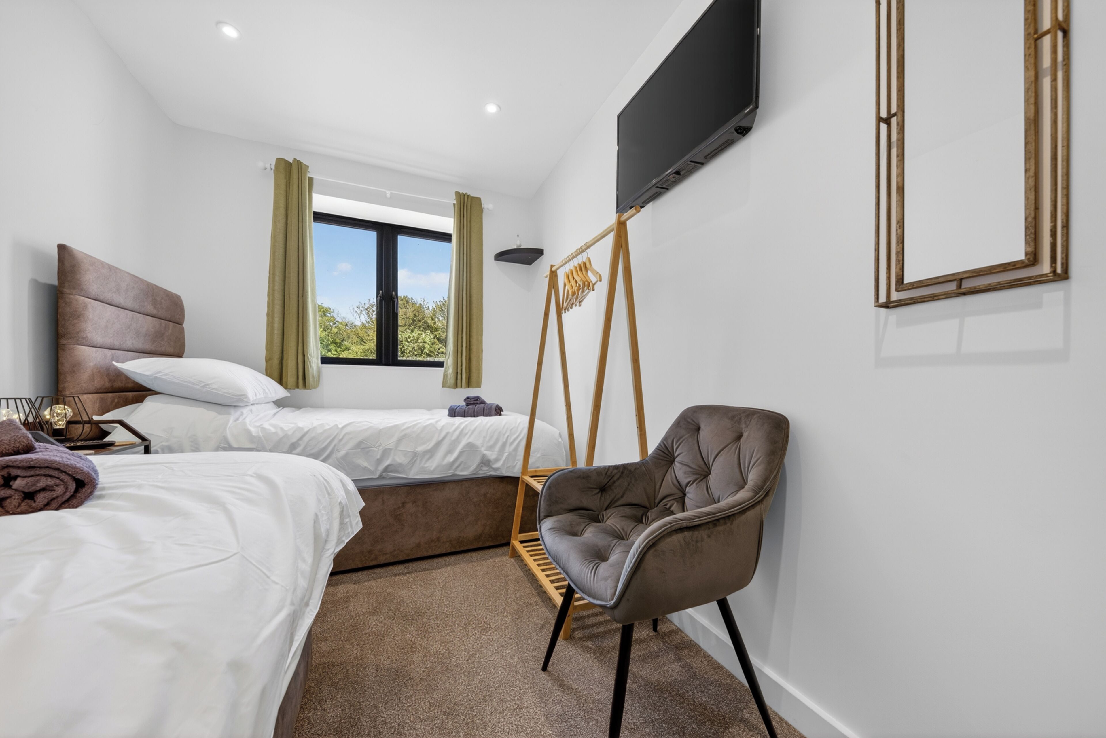 A modern hotel room with two beds, a TV, a chair, and a window with a view.