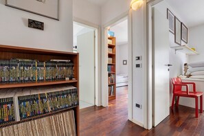 A room with a wooden floor, a bookshelf, a red chair, and a bed with a white headboard.