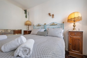 A neatly made bed with white towels, a blue headboard, a wooden nightstand with a lamp, and a small cabinet.