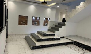 Una escalera moderna con escalones de mármol y barandilla, que conduce a un rellano con tres lámparas fijadas a la pared.