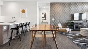 A modern kitchen with a wooden dining table, black bar stools, and a central island with a sink.