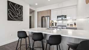 A modern kitchen with a large island, stainless steel appliances, and black bar stools.