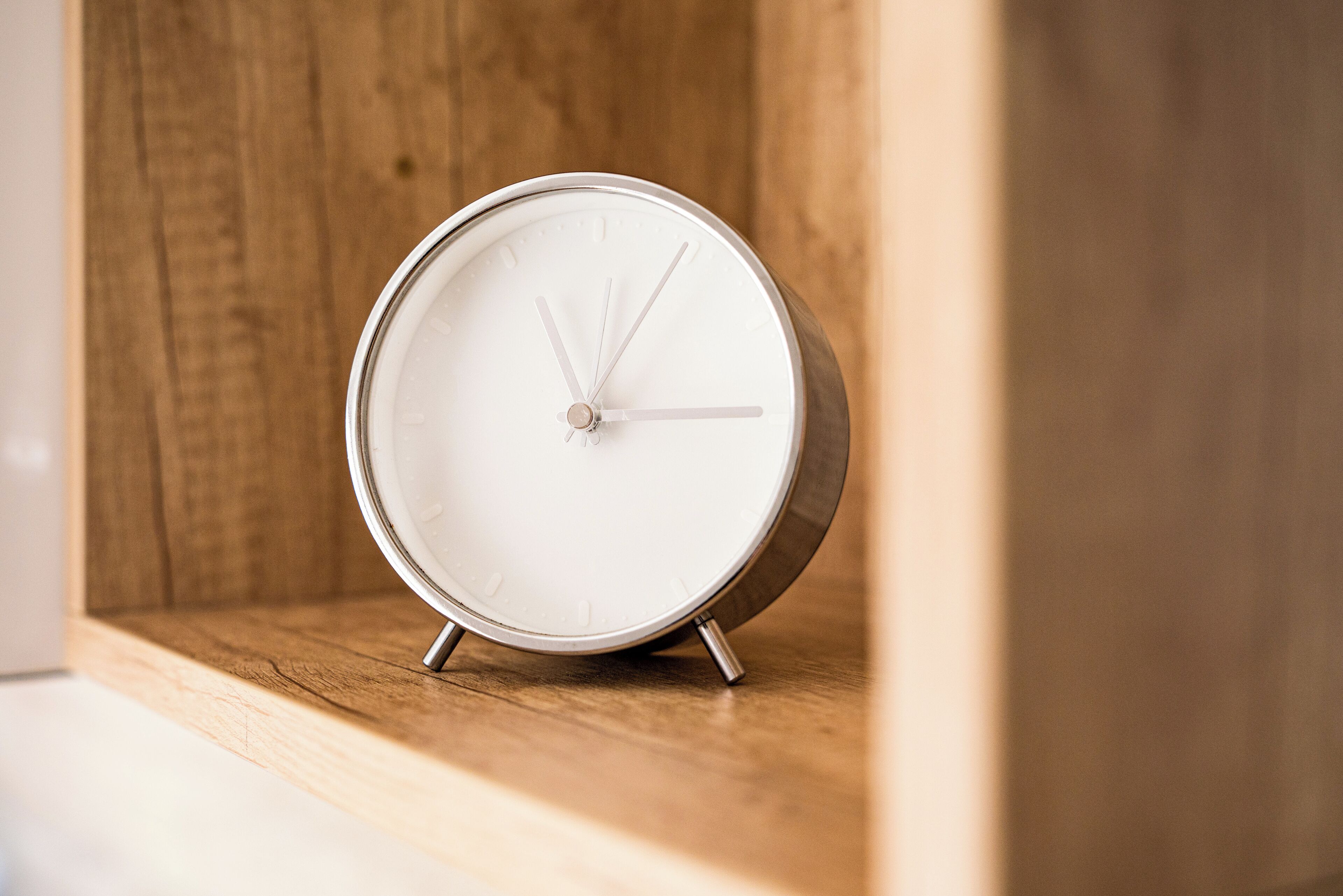Een ronde, witte analoge klok met een metalen frame, geplaatst op een houten plank.