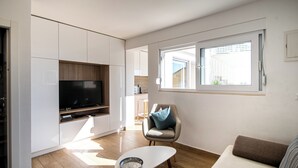 Una sala de estar moderna con una televisión de pantalla plana, un sofá, una silla y un comedor al fondo.