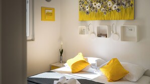 Una habitación de hotel con cama, dos mesitas de noche, una lámpara de pared, un cuadro y una ventana.