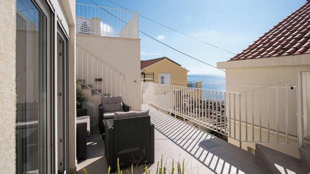 Un balcón con mobiliario exterior, vista al mar y un edificio cercano.
