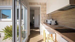 Cocina moderna con encimera de madera, taburetes blancos y vistas al exterior a través de un ventanal.