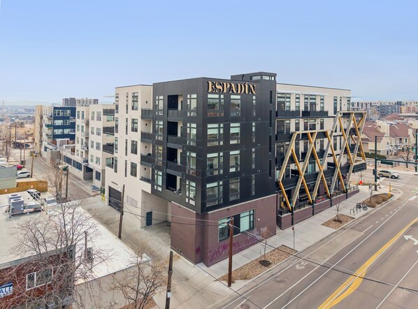 A modern building with "ESPADIN" signage, featuring a mix of balconies and large windows, located in an urban setting with visible roads and other buildings.