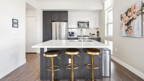 A modern kitchen with a central island, stainless steel appliances, and a bar stool seating area. - Top Floor | 1BR Corner Loft | LoHi Denver | Dog-Friendly (Denver)