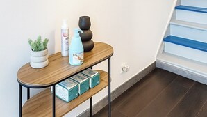 A staircase with a wooden handrail and white steps, a framed abstract painting on the wall, a small wooden shelf with decorative items, and a table with a potted plant and a bottle. - Quiet room in shared house - Lille (Lille)