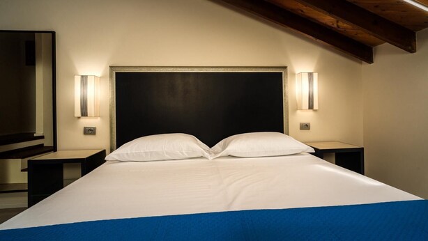 Una habitación de hotel con una cama grande, dos mesitas de noche e iluminación empotrada.