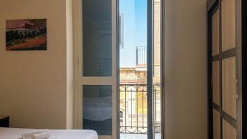Ein Schlafzimmer mit Bett, einem Bild an der Wand und einem Balkon mit Blick auf Gebäude.