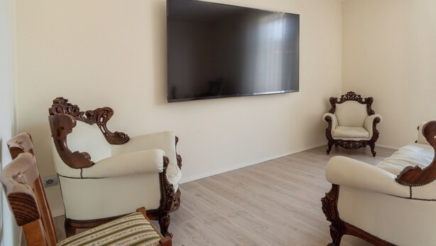 A room with two ornate chairs, a large flat-screen TV on the wall, and a light-colored wooden floor. - Viscuso house (Aci Castello)