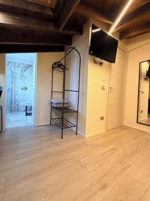 A room with a wooden floor, a black metal shelf, a flat-screen TV mounted on the wall, and a door leading to a bathroom. - Viscuso house (Aci Castello)