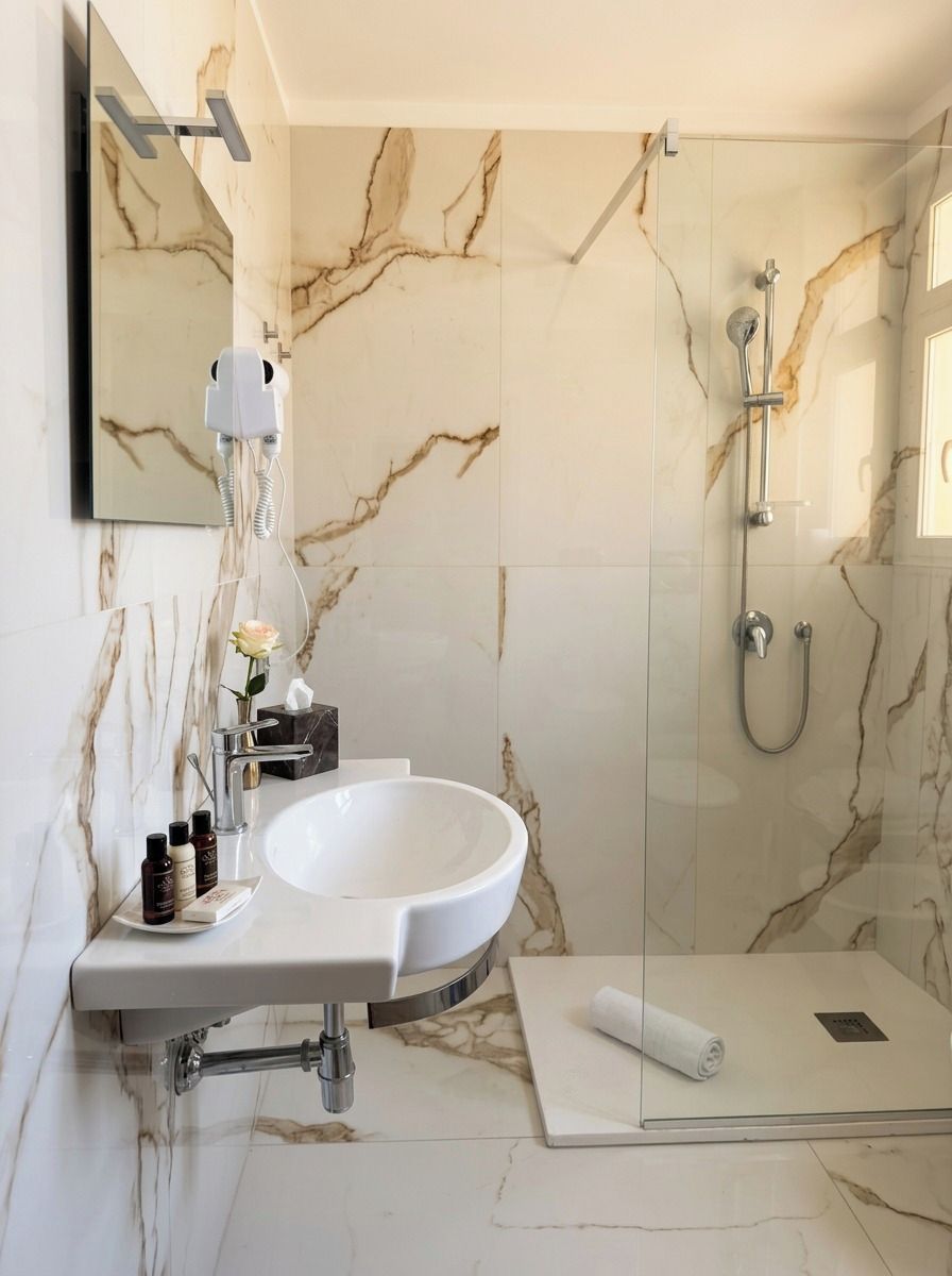 Ein Badezimmer mit einem weißen Waschbecken, einer Duschkabine aus Glas und Marmorwänden.