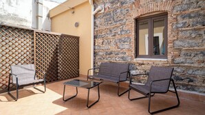 Un patio al aire libre con tres sillas y una mesa, un muro de piedra y una ventana.