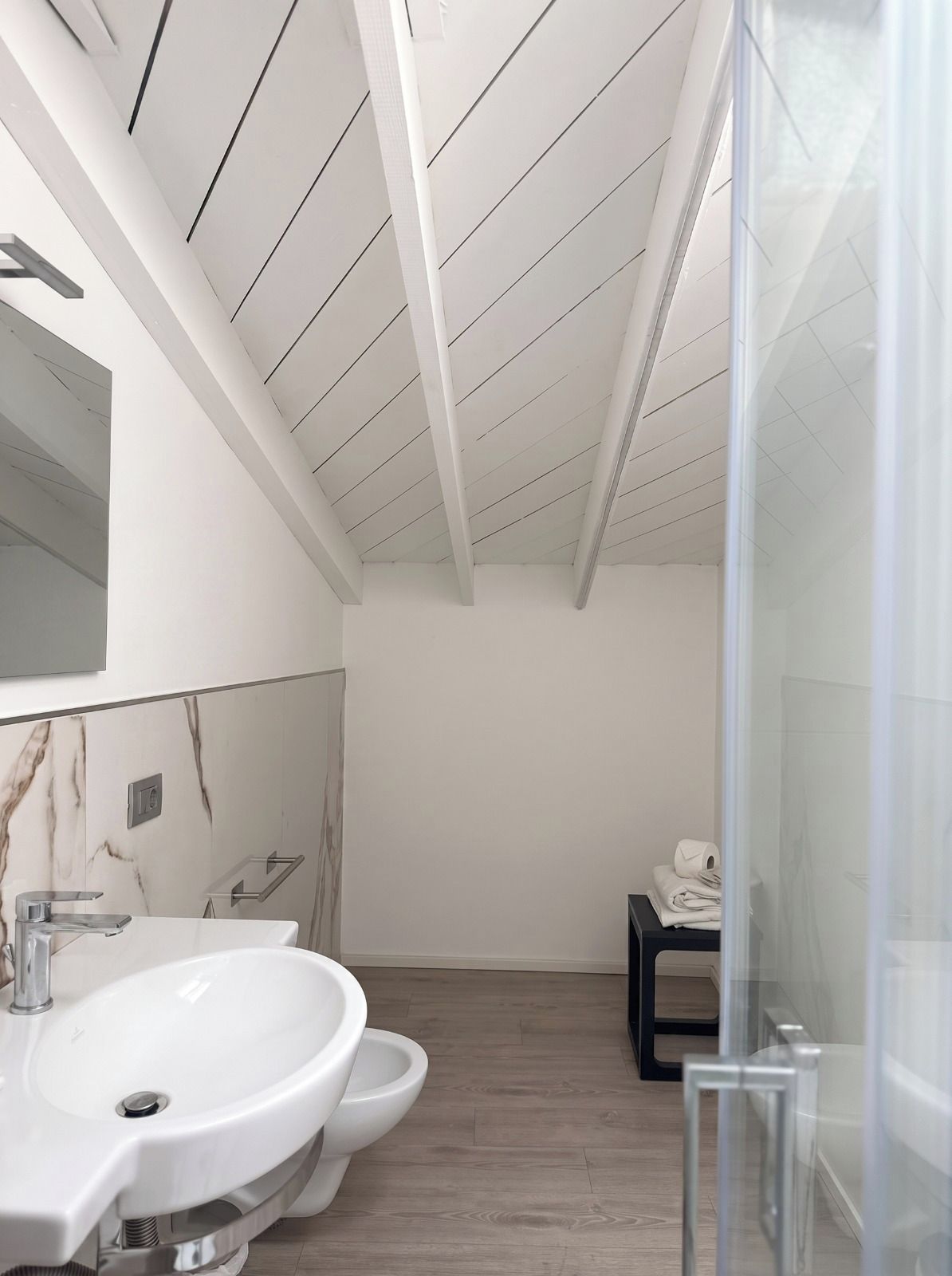 A modern bathroom with a large mirror, two sinks, a shower, and a marble wall.