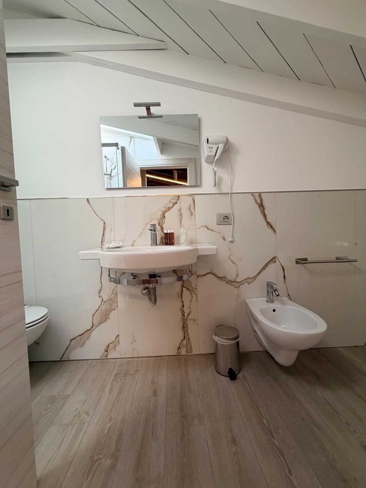 Un baño moderno con pared de mármol, lavamanos, un bidé, inodoro y espejo.