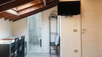 Ein Hotelzimmer mit Bett, Fernseher, Schreibtisch mit Stühlen und begehbarem Kleiderschrank.