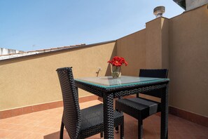 A glass-top table with wicker chairs, a vase with red flowers, and a tiled floor. - Viscuso house (Aci Castello)