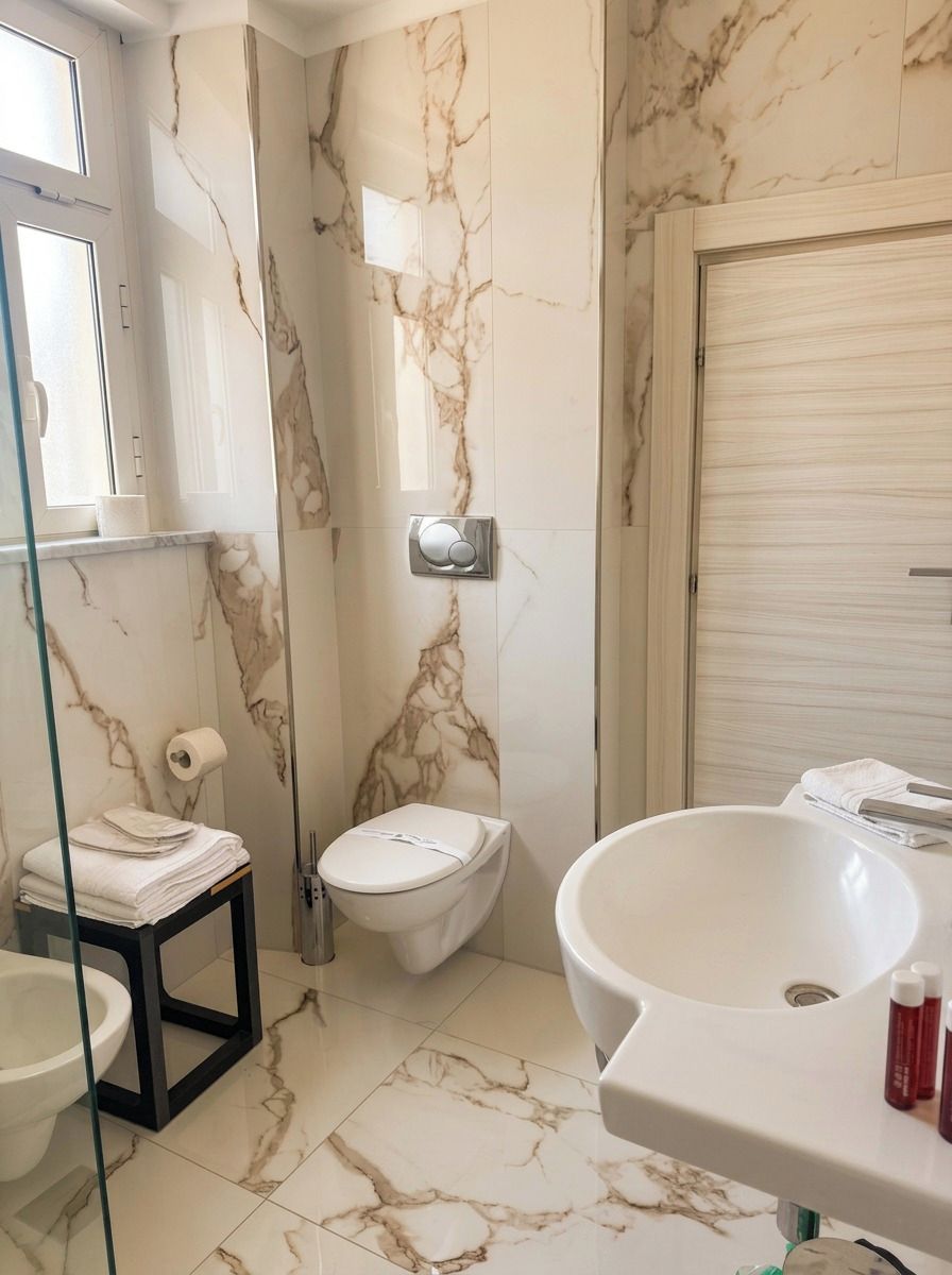Een badkamer met een marmeren wand, een toilet, een wastafel en een douchecabine van glas.