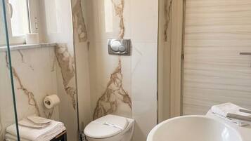 Een badkamer met een marmeren wand, een toilet, een wastafel en een douchecabine van glas.