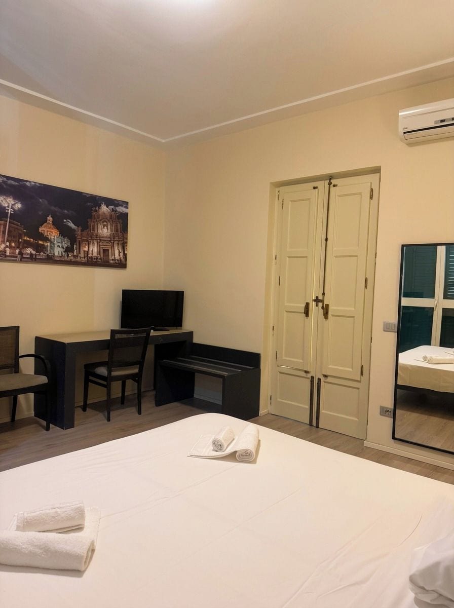 Ein Hotelzimmer mit einem Bett, einem Schreibtisch mit Stuhl, einem Fernseher, einem Kleiderschrank und einem Spiegel.