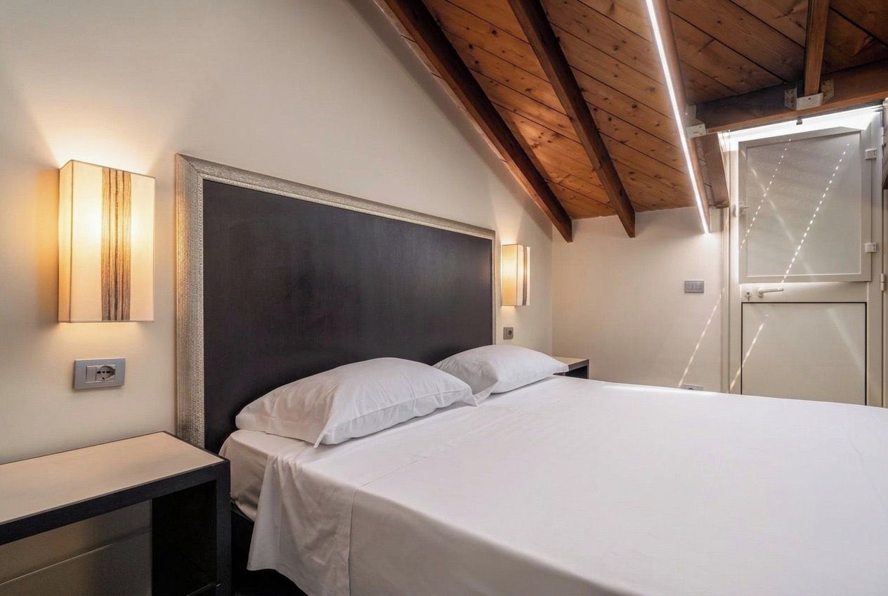Un dormitorio con cama, mesitas de noche e iluminación en la pared.