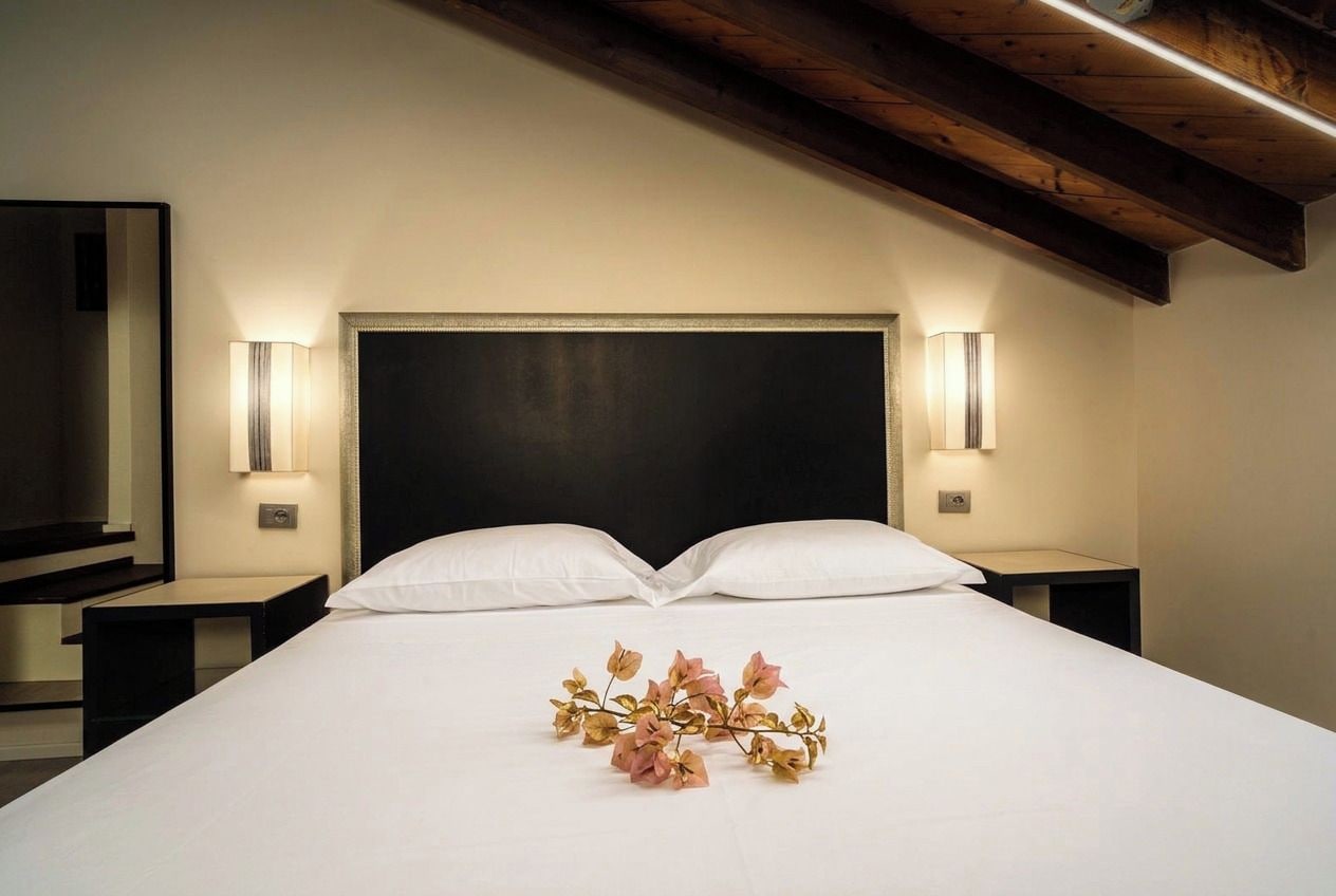 A hotel room with a large bed, two bedside tables, and a dark headboard.