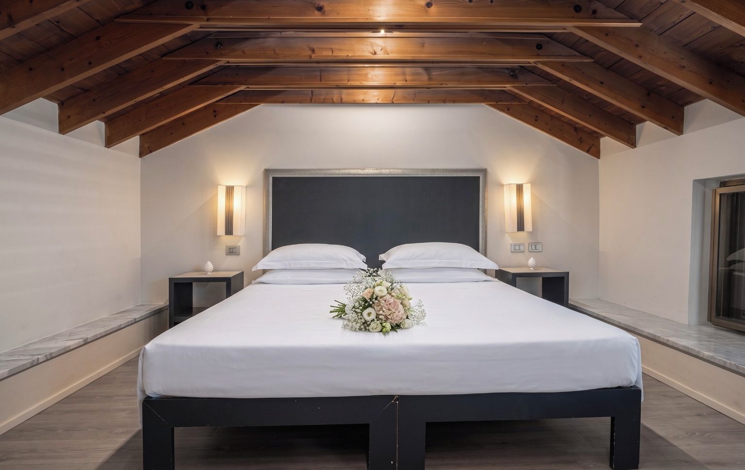 A bedroom with a large bed, two bedside tables, and a wooden ceiling.