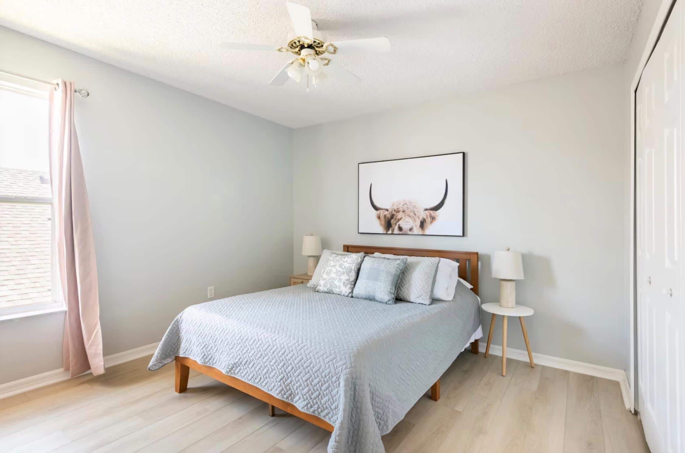 Une chambre à coucher comprenant un lit, des tables de chevet, un ventilateur de plafond et un tableau représentant un taureau, accroché au mur.