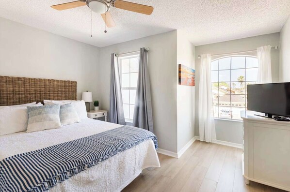 A bedroom with a bed, a ceiling fan, a TV, a window with curtains, and a view of the outside. - Theme Park Days & Sunshine Stays (Kissimmee)