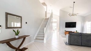 Una sala de estar moderna con una escalera, un sofá gris, una mesa consola de madera, una planta en maceta y un espejo grande.