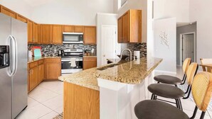 Una cocina moderna con armarios de madera, encimeras de granito, un refrigerador de acero inoxidable y una isla central con asientos.