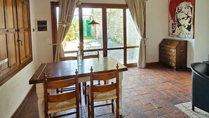 Ein rustikales Zimmer mit Holztisch und -stühlen, einem Steinkamin und Blick durch eine Glastür.